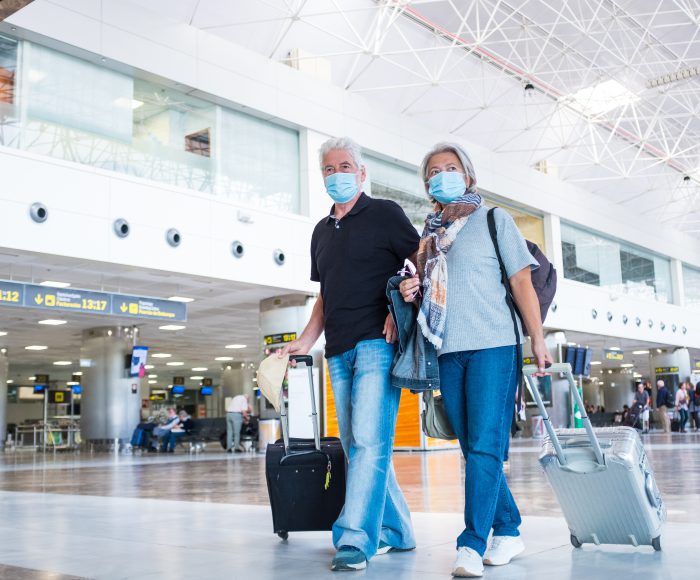 couple of two seniors or mature people walking in the airport going to their gate and take their flight wearing medical mask to prevent virus like coronavirus or covid-19 – carrying luggage or trolley